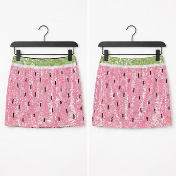 Two pink sequined mini skirts with a watermelon print pattern, hanging on black hangers against a white background.