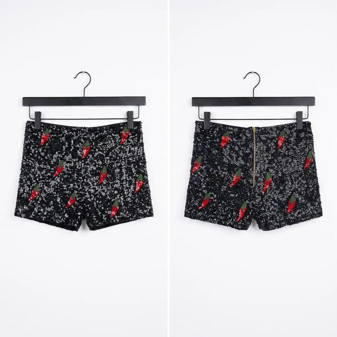 Black shorts with a white speckled pattern and red chili pepper prints, shown from both front and back views on black hangers against a white background.