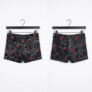 Black shorts with a white speckled pattern and red chili pepper prints, shown from both front and back views on black hangers against a white background.
