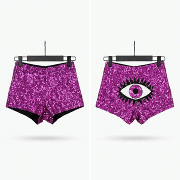 Two pairs of high-waisted, sparkly magenta-purple sequin shorts displayed side by side on black hangers against a light gray background. The left pair has a solid sequin texture, and the right pair features a large black and white eye graphic on the front.
