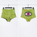 A pair of high-waisted, sequined shorts shown from both front and back views on black hangers against a white background. The shorts feature a lime green sequined texture, with the back view displaying a large embroidered eye motif in pink, black, and white.